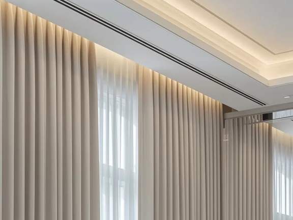 Floor-length curtains on a ceiling track beside a lit cove
