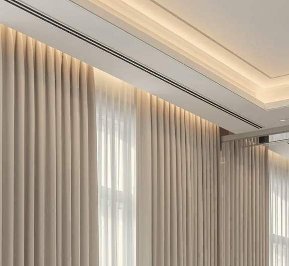 Floor-length curtains on a ceiling track beside a lit cove