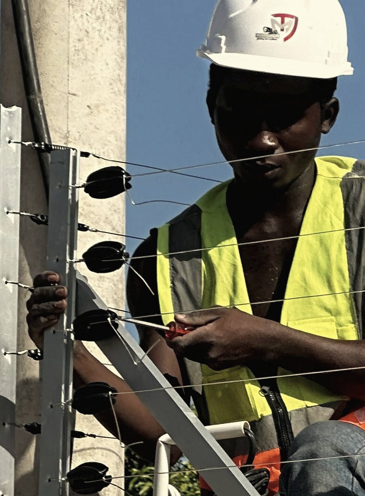 A technician in a hard hat and high-visibility vest connecting the wires of an electric fence