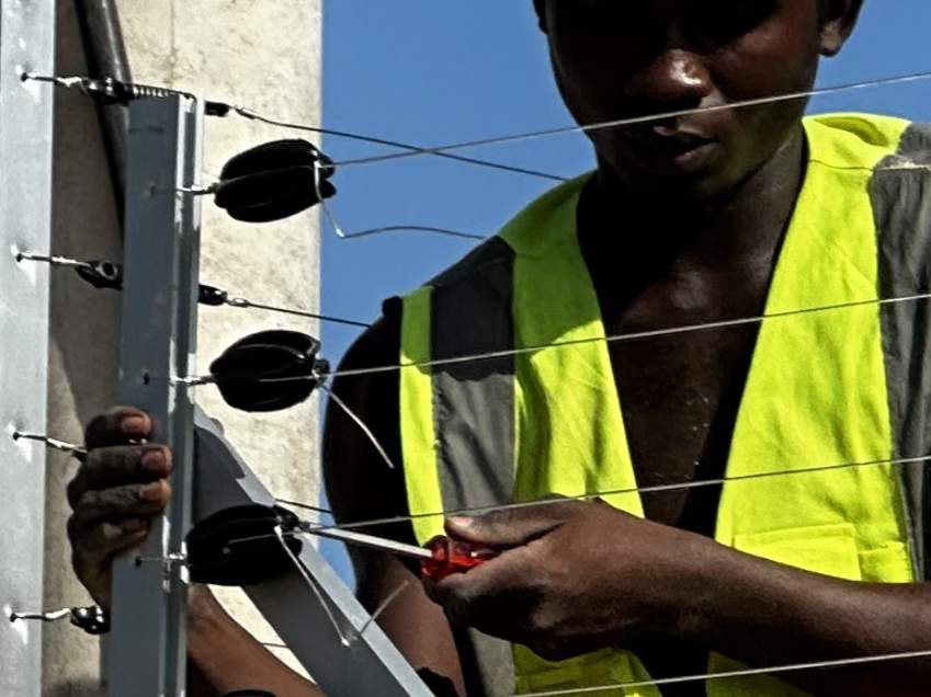 A technician in a hard hat and high-visibility vest connecting the wires of an electric fence